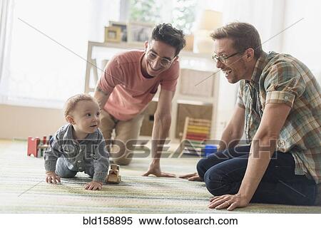 Caucasian gay fathers and baby playing in living room View Large Photo Image Stock Photography - Caucasian gay fathers and baby playing in living room. Fotosearch