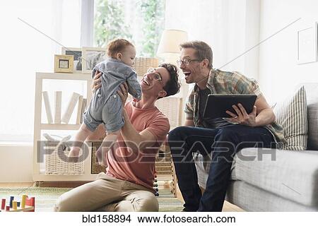 Caucasian gay fathers and baby relaxing in living room View Large Photo Image Picture - Caucasian gay fathers and baby relaxing in living room. Fotosearch