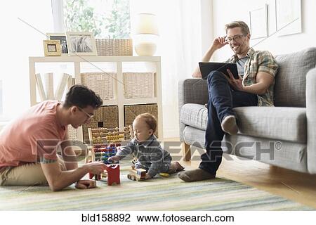 Caucasian gay fathers and baby relaxing in living room View Large Photo Image Stock Image - Caucasian gay fathers and baby relaxing in living room. Fotosearch