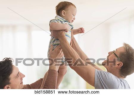 Stock Image - Caucasian gay fathers holding baby. Fotosearch