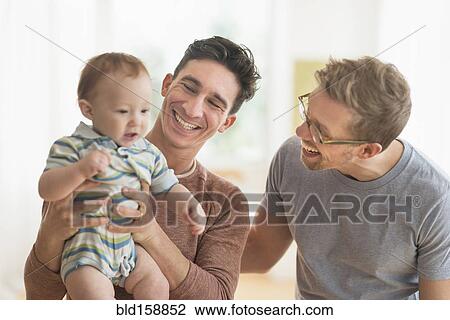Stock Image - Caucasian gay fathers holding baby. Fotosearch