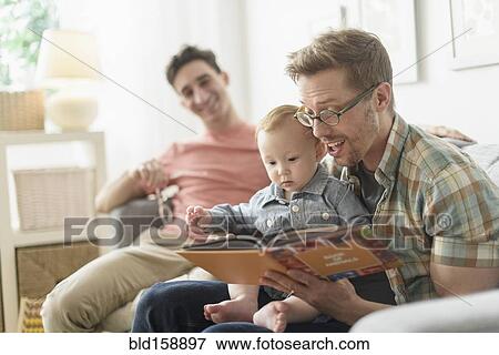 Stock Photo - Caucasian gay fathers reading to baby in living room. Fotosearch