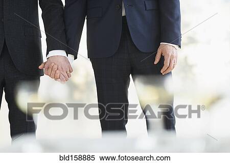 Stock Photography - Caucasian gay grooms holding hands at wedding. Fotosearch