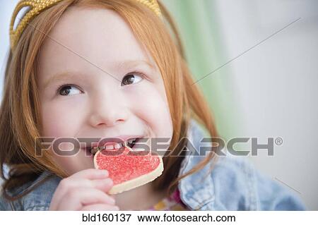 Stock Photo - Caucasian girl eating heart-shape cookie. Fotosearch