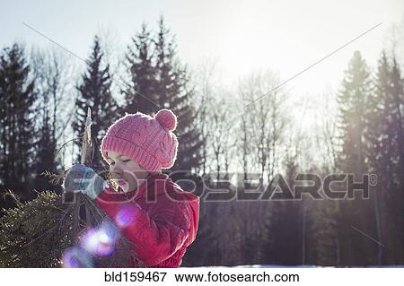 Stock Photo - Caucasian girl holding tree branches in snowy field. Fotosearch