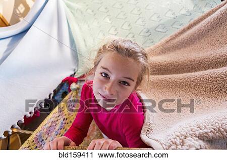 Stock Image - Caucasian girl playing in blanket fort. Fotosearch
