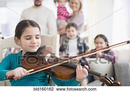 Stock Image - Caucasian girl playing violin in living room. Fotosearch