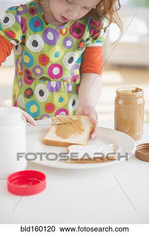 Stock Image - Caucasian girl spreading peanut butter on bread. Fotosearch