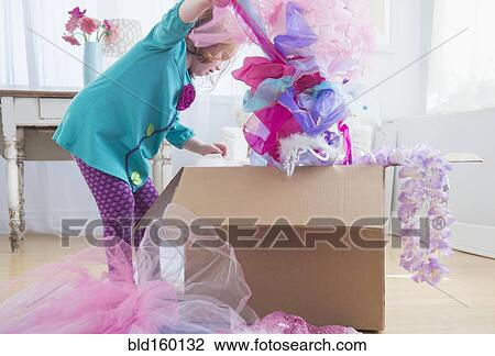 Stock Image - Caucasian girl unpacking dress-up clothes from box. Fotosearch