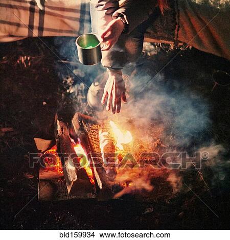 Picture - Caucasian girl warming hands above campfire. Fotosearch