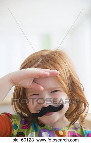Stock Image - Caucasian girl wearing fake mustache. Fotosearch