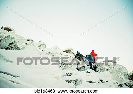 Stock Photo - Caucasian hiker climbing snowy rock formations. Fotosearch