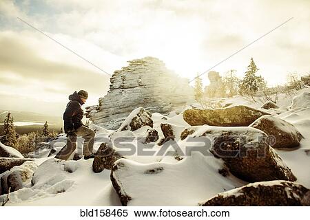 Stock Photography - Caucasian hiker climbing snowy rock formations. Fotosearch