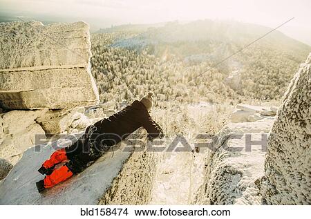 Picture - Caucasian hiker laying on snowy rock formations. Fotosearch