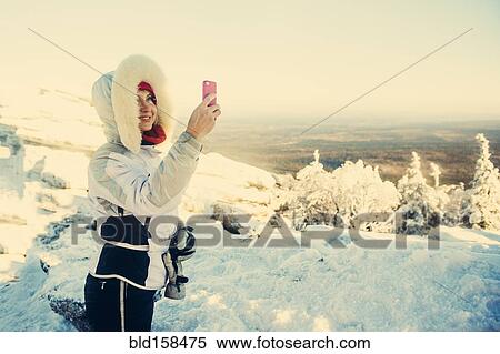 Stock Photography - Caucasian hiker taking cell phone photograph in snow. Fotosearch