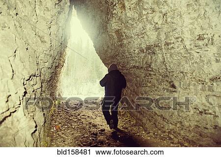 Stock Image - Caucasian hiker walking in rocky cave. Fotosearch