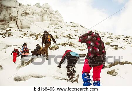 Stock Image - Caucasian hikers climbing snowy rock formations. Fotosearch