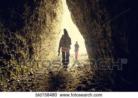 Stock Image - Caucasian hikers walking in rocky cave. Fotosearch