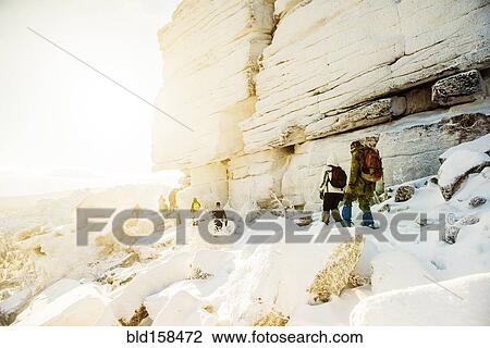 Stock Image - Caucasian hikers walking on snowy rock formations. Fotosearch