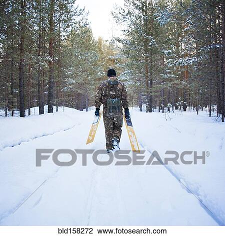 Stock Image - Caucasian man carrying skis on snowy road. Fotosearch