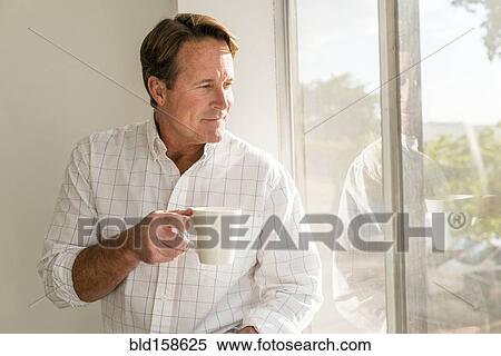 Stock Photography - Caucasian man drinking cup of coffee near window. Fotosearch