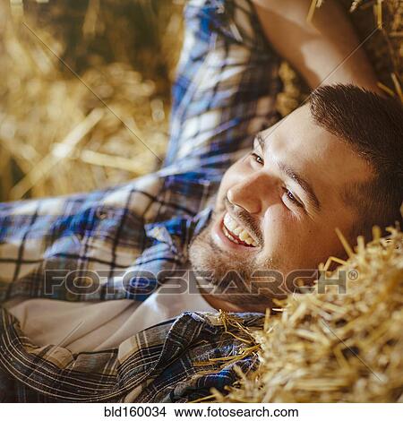 Picture - Caucasian man laying on haystacks. Fotosearch