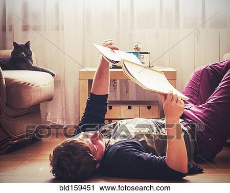 Stock Image - Caucasian man reading on living room floor. Fotosearch