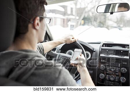 Stock Image - Caucasian man using cell phone and driving car. Fotosearch