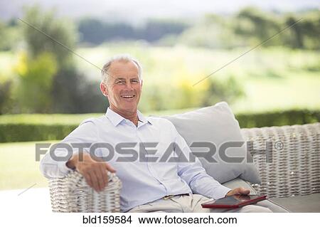 Picture - Caucasian man using digital tablet on sofa outdoors. Fotosearch