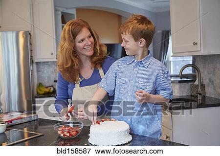 Stock Photo - Caucasian mother and son decorating cake in kitchen. Fotosearch