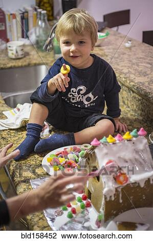 Stock Image - Caucasian mother and son making gingerbread house in kitchen. Fotosearch