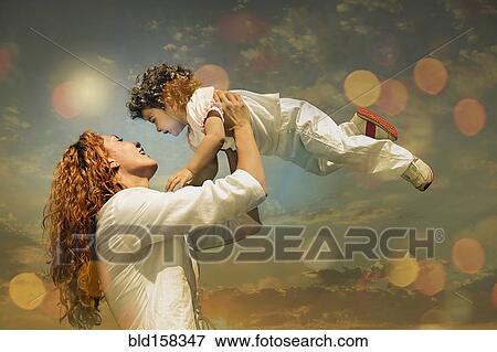 Stock Photo - Caucasian mother lifting son under sunny sky. Fotosearch