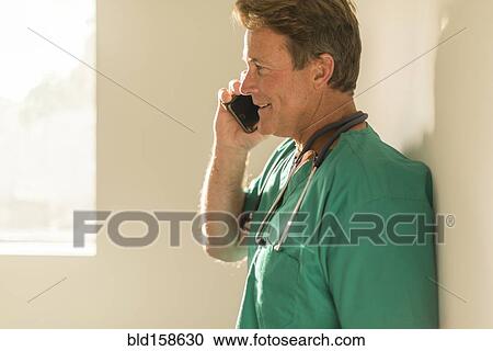 Stock Image - Caucasian nurse talking on cell phone near window. Fotosearch