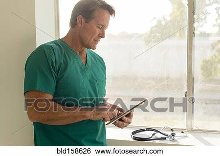 Stock Photograph - Caucasian nurse using digital tablet near window. Fotosearch