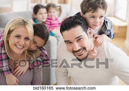 Stock Photography - Caucasian parents carrying children piggyback in living room. Fotosearch