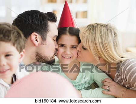 Picture - Caucasian parents kissing daughter at birthday party. Fotosearch