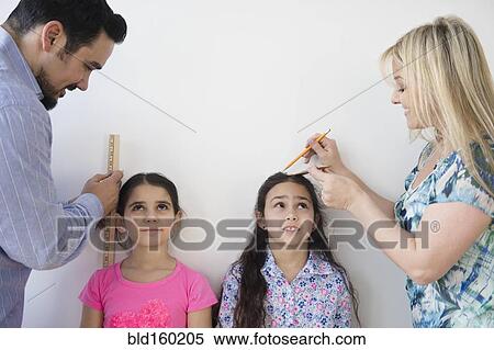 Stock Photography - Caucasian parents measuring height of daughters on wall. Fotosearch