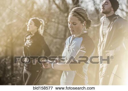 Stock Photo - Caucasian runner checking fitness watch in forest. Fotosearch