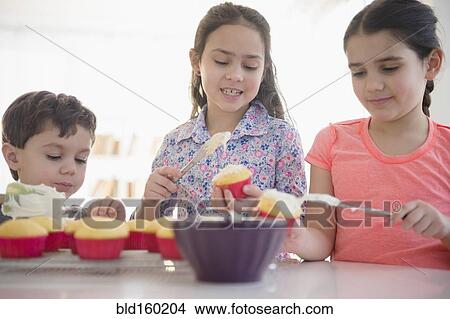 Caucasian siblings spreading frosting on cupcakes View Large Photo Image Picture - Caucasian siblings spreading frosting on cupcakes. Fotosearch