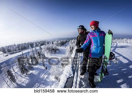 Stock Photo - Caucasian snowboarders standing on snowy mountaintop. Fotosearch