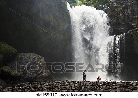 Stock Photo - Caucasian tourists admiring waterfall in jungle. Fotosearch