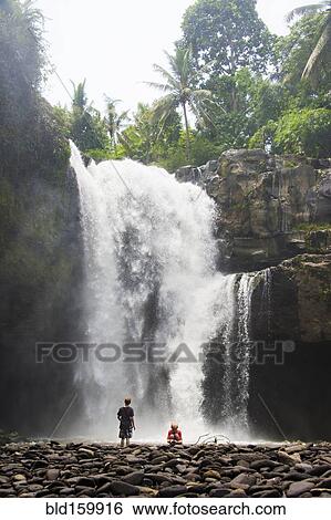 Stock Photograph - Caucasian tourists admiring waterfall in jungle. Fotosearch
