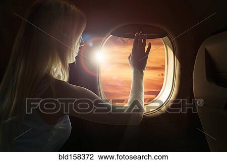 Stock Image - Caucasian woman admiring sunset from airplane window. Fotosearch
