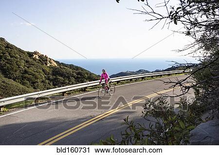 Stock Image - Caucasian woman biking on remote mountain road. Fotosearch