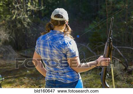 Stock Photo - Caucasian woman carrying rifle in forest. Fotosearch
