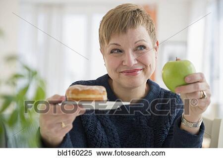 Stock Photography - Caucasian woman choosing between donut and apple. Fotosearch