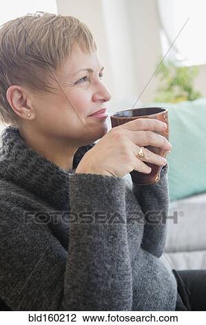 Stock Image - Caucasian woman drinking cup of coffee on sofa. Fotosearch