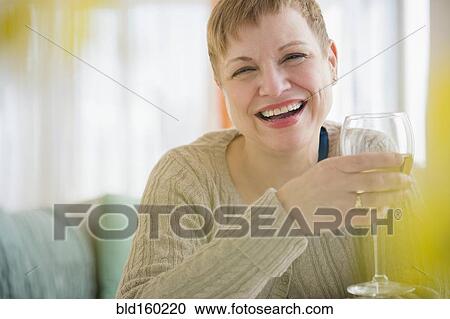 Stock Image - Caucasian woman drinking glass of wine on sofa. Fotosearch