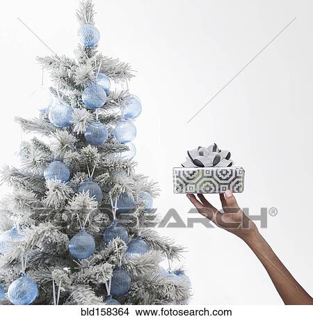 Picture - Caucasian woman holding wrapped gift near Christmas tree. Fotosearch