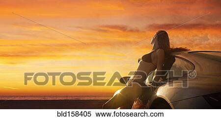 Stock Photography - Caucasian woman in bikini leaning on sports car at sunset. Fotosearch